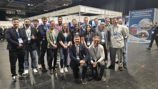 Group photo of researchers from TU Dortmund University, RWTH Aachen University, and Ruhr University Bochum (RUB) at the 6GEM+ exhibition booth during IEEE ICC 2026.